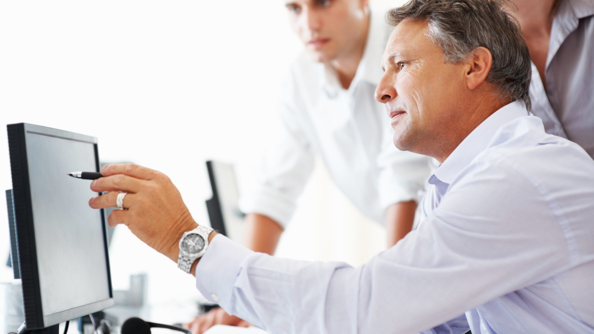 Business project Mature business man discussing project with his colleagues and pointing at computer screen